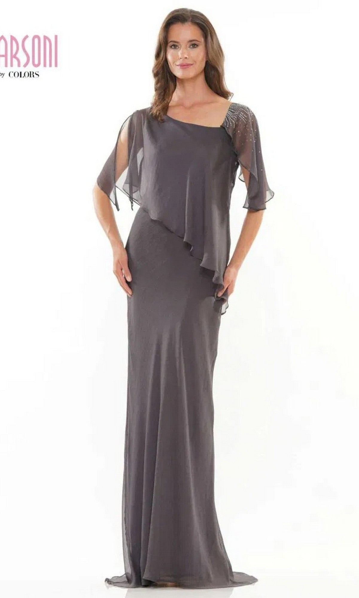 A woman stands against a plain white background wearing the Marsoni M313, a floor-length, charcoal formal dress with chiffon fabric, sheer asymmetrical overlay, and short flutter sleeves.